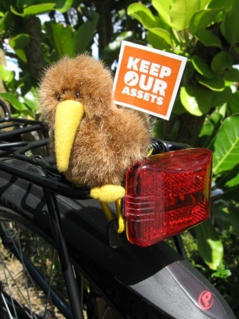 A Keep Our Assets flag with the help of a brave kiwi riding pillion on Wellington's streets